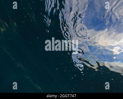 Sun light beams shining from above coming through the deep blue water causing a reflections curtain. Underwater ocean waves oscillate and flow. Scene Stock Photo