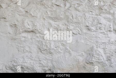 Close-up of old, rough and plastered stone block wall painted in white, front view. Abstract full frame textured background. Copy space. Stock Photo