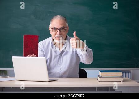 Old teacher in front of green board Stock Photo