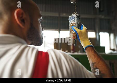 Engineer in uniform using crane controller hanging from ceiling in a factory Stock Photo