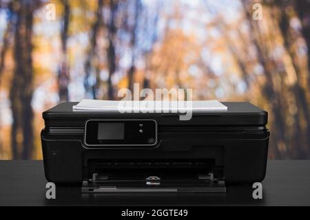 Compact laser printer on black desk against blurred background Stock Photo