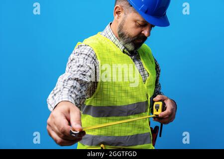 Male builder holding measuring roulette against blue background Stock Photo