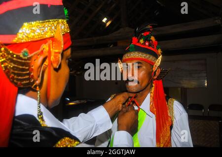 A player of Jathilan or Kuda Lumping, a traditional art, is helping his friend tighten the headband. Stock Photo