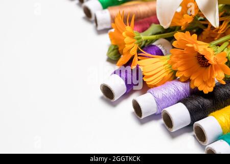 Multicolored threads and flowers on a white background with copy space for text. Greeting card for a seamstress, tailor, needlewoman and atelier for Stock Photo