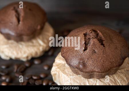 Two homemade chocolate muffins on parchment with coffee beans. Dark wooden background, closeup, selective focus Stock Photo
