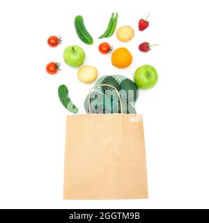 Assorted fruits and vegetables falling into a craft paper shopping bag isolated on white. Creative organic groceries flat lay. Stock Photo