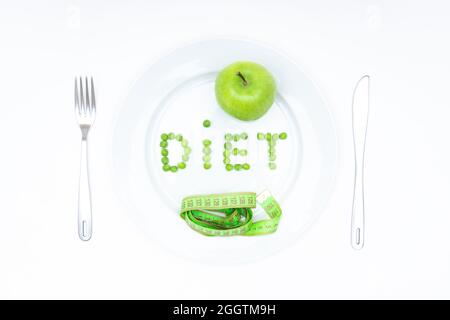 Word DIET arranged of garden peas and served on a large white plate with a fresh green apple, a soft measuring tape, knife and fork isolated on white. Stock Photo