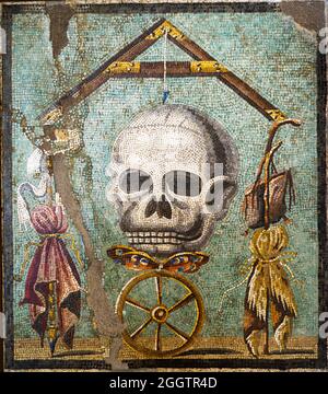 Memento Mori Mosaic emblema in opus vermiculatum made from polychrome tesserae. The mosaic depicts the allegory of death which levels distinctions between human beings. At the top of the composition there is a plumb-bob with its plumb-line whose axis is death in the form of a skull; below there is a butterfly, the soul, on a wheel, symbolising Fortune: between the arms of the plumb-blob are the symbols of poverty on the right (the saddlebag, the beggar's stick and the cloak) and the symbols of wealth on the left (the sceptre, purple and the crown).  Pompeii, casa bottega (shop house) - Italy Stock Photo