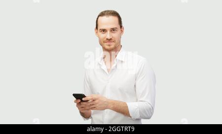 Confident and positive man with phone. Man holds smartphone in both hands and communicate via social network. Using a mobile cell in everyday life. Ho Stock Photo