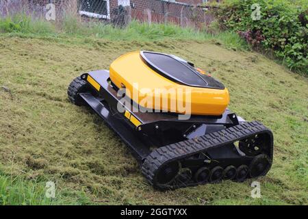 Remote controlled agricultural grass and bush cutter on a steep grassy bank. Robotic lawn mower.
