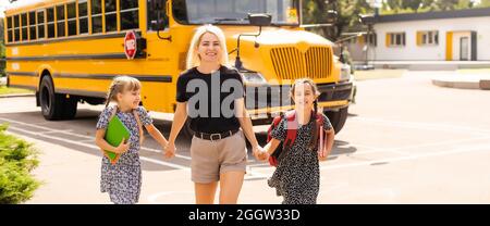 Back to school. Pupils of primary school near school bus. Happy children ready to study. little girls with mom going to bus Stock Photo