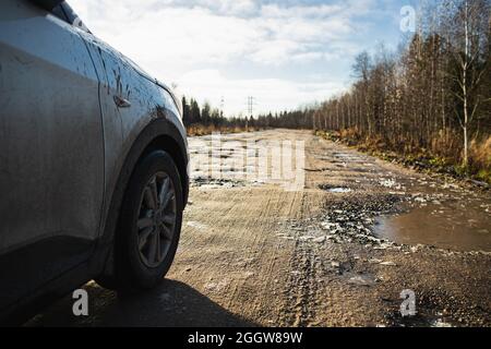 Car on Autumn dirty gravel road with hoarfrost covered potholes. It has some surface damage, needs maintenance, hole patching, dust binding and draggi Stock Photo