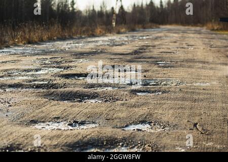 Autumn dirty gravel road with hoarfrost covered potholes. It has some surface damage, needs maintenance, hole patching, dust binding and dragging. The Stock Photo