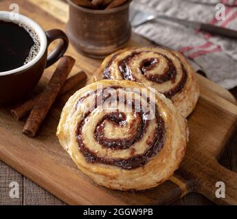 Glazed cinnamon rolls with cup of coffee and cinnamon sticks on a wooden cutting board Stock Photo