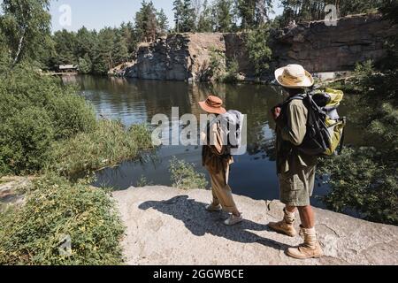 Multiethnic family with backpacks standing on rock near lake Stock Photo