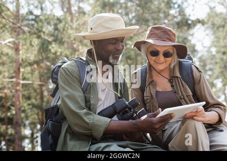 Interracial couple of tourists using digital tablet in forest Stock Photo