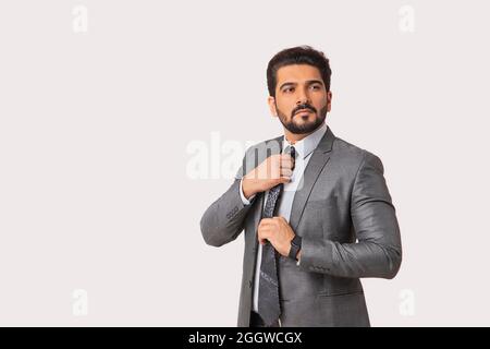 Portrait of a man in formal business suit setting his necktie against plain background. Stock Photo