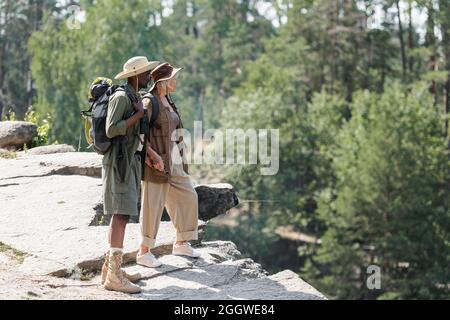 Side view of multiethnic hikers holding hands on rock in forest Stock Photo