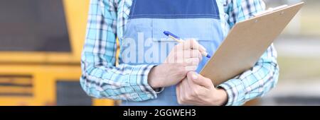 Woman builder in overalls holding clipboard and ballpoint pen closeup Stock Photo