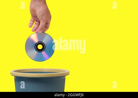 Old, outdated CD in your hand is thrown into trash.Yellow background Stock Photo