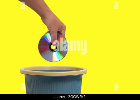 Old, outdated CD in your hand is thrown into trash.Yellow background Stock Photo