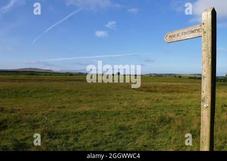 A Public Footpath sign pointing across a field towards a distant hill, Cumbria, England, United Kingdom Stock Photo