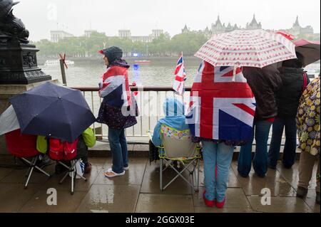 Spectators waiting in the rain for The Thames Diamond Jubilee Pageant to pass the South Bank, London. The Pageant was made up of hundreds of boats that sailed from Battersea Bridge to Tower Bridge to celebrate Queen Elizabeth II's 60 years on the throne. Millions of people lined the banks of the Thames to watch the spectacle.  South Bank, London, UK.  3 Jun 2012 Stock Photo