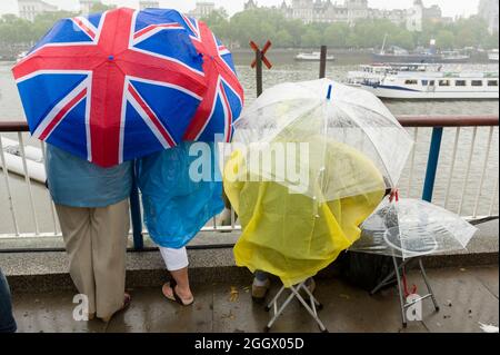 Spectators waiting under  Union Jack umbrellas in the rain for The Thames Diamond Jubilee Pageant to pass the South Bank, London. The Pageant was made up of hundreds of boats that sailed from Battersea Bridge to Tower Bridge to celebrate Queen Elizabeth II's 60 years on the throne. Millions of people lined the banks of the Thames to watch the spectacle.  South Bank, London, UK.  3 Jun 2012 Stock Photo