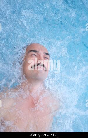 Happy mature asian man laying on water relax in outdoor thermal pool with hydromassage. Stock Photo