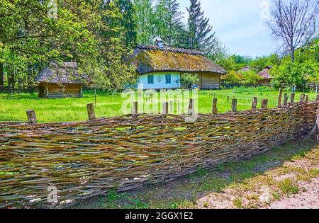 PEREIASLAV, UKRAINE - MAY 22, 2021: The scenic village hata house of traditional Ukrainian farmstead behind the old wicker fence, Pereiaslav Scansen, Stock Photo