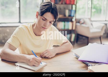 Portrait of attractive focused guy writing list essay doing homework preparing academic test exam indoors Stock Photo