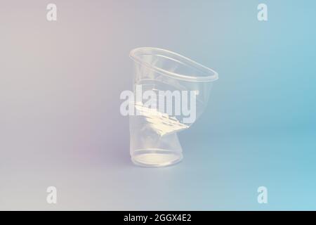 Crushed disposable glass on a gradient pink blue background. Recycling concept. Stock Photo