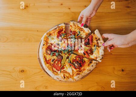 Overhead shot of two female hands taking slices from the whole pizza Stock Photo