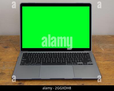 A modern laptop computer is shown isolated on an old, wood office desk, with a green screen on the monitor to add your own graphics. Stock Photo