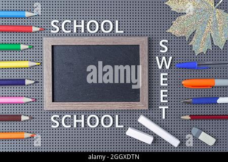 Black chalk board and school supplies on a gray background with the inscription "School sweet school". Stock Photo