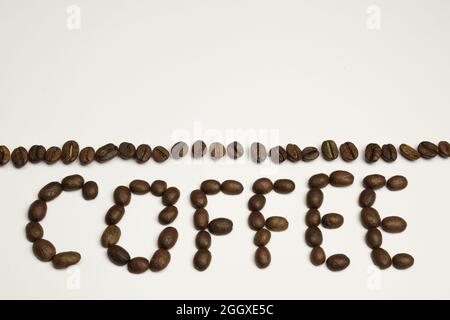 The word COFFEE is laid out on a white background with coffee beans. Above it is a strip of coffee beans Stock Photo