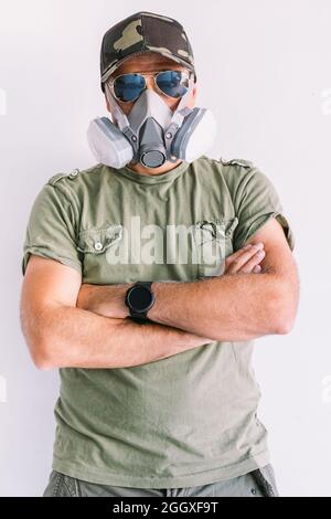 Military man wearing camouflage cap and sunglasses, with protection mask, on a white wall Stock Photo