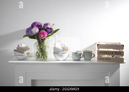 kitchen utensils, cups, bowls, bottles, storage items, a bouquet of asters are on a white dresser Stock Photo
