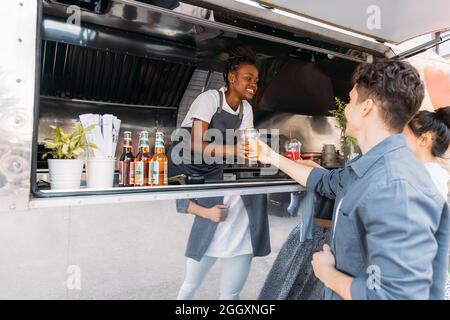 Smiling male and female customers receiving drinks from saleswoman. Young entrepreneur working in her a food truck. Stock Photo