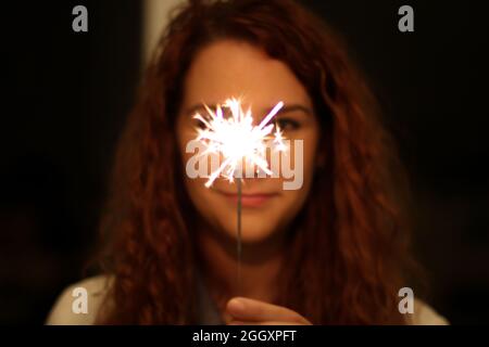 Blurred Young redhead Hispanic and Caucasian holding a sparkler in focus standing in the dark outside