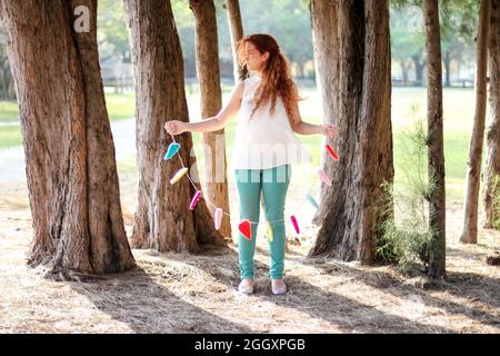 Young Redhead woman standing in nature amongst trees holding a garland made of hearts to symbolize love and romance. Stock Photo