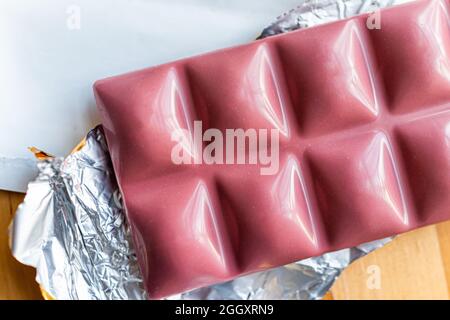 Closeup of pink trendy ruby chocolate bar on plate with aluminum foil wrapper and packaging macro flat top view Stock Photo