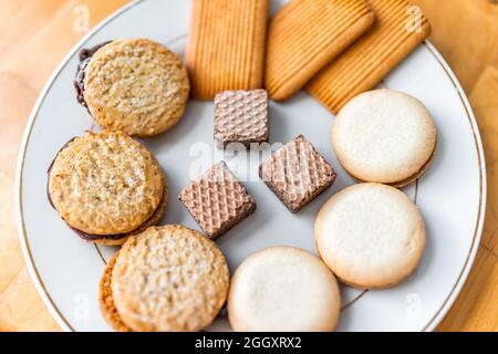 Flat top view of assortment of snacks of gourmet chocolate cookies with wafers and sweet biscuit with filling on white plate macro closeup Stock Photo