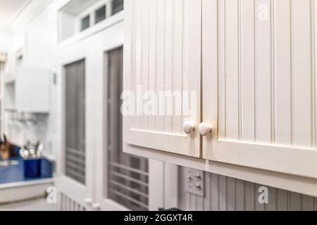 Modern vintage beach cottage style white wooden cabinets in house home closeup with background of kitchen room and window Stock Photo