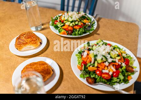 Two baked pastries croissants on plates with chocolate filling, glasses of water and salads with vegetables for dinner and dessert Stock Photo