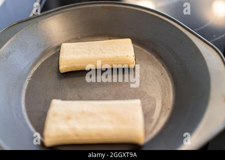 Two white frozen storebought pastry unbaked croissants on baking tray pan rising from yeast overnight closeup Stock Photo