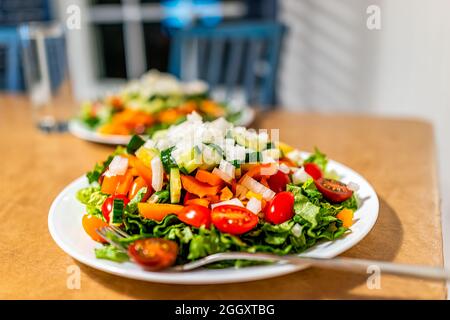 Closeup of two fresh chopped salads on white plates with lettuce, tomatoes bell peppers and bokeh background Stock Photo