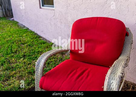Closeup of one wicker outdoor armchair chair outside with red cushion at front yard or backyard with green grass lawn at sunset in Naples, Florida Stock Photo