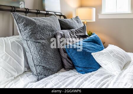 Closeup of decorative pillows cushions in shams and white bedding comforter duvet on bed in bedroom with illuminated lamp on nightstand and bright nat Stock Photo