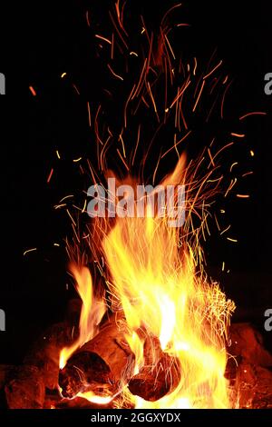 A burning fire, wooden logs, red sparks and yellow flames on a dark background Stock Photo